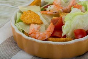 Caesar salad with shrimps in a bowl on wooden background photo