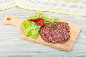 Sliced salami on wooden board and wooden background photo