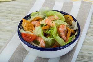 Caesar salad with shrimps in a bowl on wooden background photo