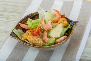 Caesar salad with shrimps in a bowl on wooden background photo