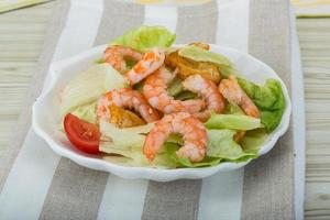 Caesar salad with shrimps in a bowl on wooden background photo