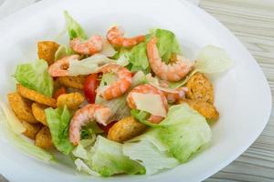 Caesar salad with shrimps in a bowl on wooden background photo