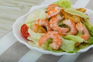 Caesar salad with shrimps in a bowl on wooden background photo