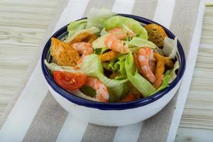 Caesar salad with shrimps in a bowl on wooden background photo