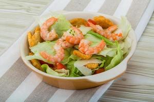 Caesar salad with shrimps in a bowl on wooden background photo