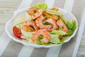 Caesar salad with shrimps in a bowl on wooden background photo