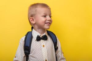 Back to school. A blond smiling boy with a backpack on a yellow background looks away. Copy space. Education. Banner photo