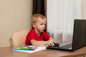 aprendizaje a distancia en línea. el niño mira cuidadosamente la computadora portátil y estudia la lección de dibujo en línea en Internet. escuela en línea. foto