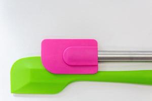 Two silicone spatulas, one is green and the another is pink lay on white background photo