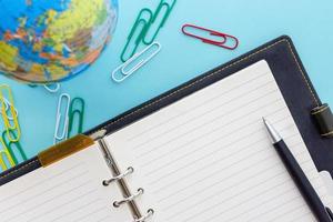 Leather ring planner with black pen, globe and colorful clips open on blue workspace photo