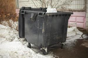 Black garbage can on street. Dirty container in ghetto. Waste garbage. photo