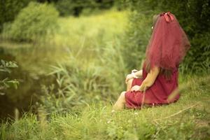 Girl on nature. Girl in dress sitting in grass. Red dress on woman. photo