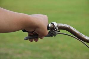 A young guy holds handle bars of vintage bike which parked on the meadow background, soft and selective focus on hand. photo