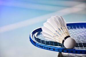 volante de bádminton blanco crema y raqueta con sombreado de luz de neón en el suelo verde en la cancha de bádminton cubierta, fondo de bádminton borroso, espacio para copiar. foto