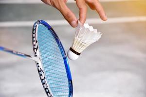 Badminton player holds racket and white cream shuttlecock in front of the net before serving it to another side of the court. photo