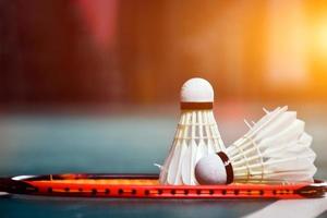 volante de bádminton blanco crema y raqueta con sombreado de luz de neón en el suelo verde en la cancha de bádminton cubierta, fondo de bádminton borroso, espacio para copiar. foto