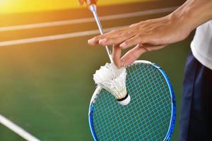 Badminton player holds racket and white cream shuttlecock in front of the net before serving it to another side of the court. photo