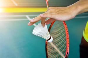 Badminton player holds racket and white cream shuttlecock in front of the net before serving it to another side of the court. photo