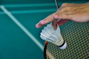 Badminton player holds racket and white cream shuttlecock in front of the net before serving it to another side of the court. photo