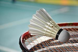 Cream white badminton shuttlecock and racket with neon light shading on green floor in indoor badminton court, blurred badminton background, copy space. photo