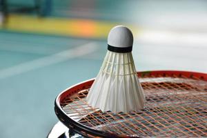 volante de bádminton blanco crema y raqueta con sombreado de luz de neón en el suelo verde en la cancha de bádminton cubierta, fondo de bádminton borroso, espacio para copiar. foto