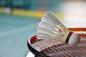 volante de bádminton blanco crema y raqueta con sombreado de luz de neón en el suelo verde en la cancha de bádminton cubierta, fondo de bádminton borroso, espacio para copiar. foto