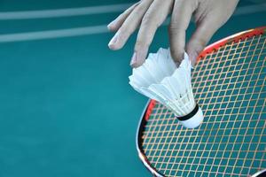 Badminton player holds racket and white cream shuttlecock in front of the net before serving it to another side of the court. photo