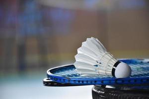 Cream white badminton shuttlecock and racket with neon light shading on green floor in indoor badminton court, blurred badminton background, copy space. photo