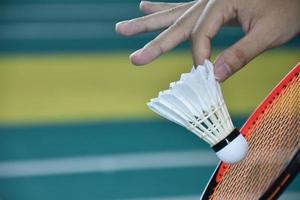 Badminton player holds racket and white cream shuttlecock in front of the net before serving it to another side of the court. photo