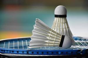 Cream white badminton shuttlecock and racket with neon light shading on green floor in indoor badminton court, blurred badminton background, copy space. photo