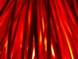 Blurred defocused Halloween horizontal background. Bundle of hay or straw or brushwood or sticks backlighted by red lamp like a fire. Dark red and orange vertical lines. photo