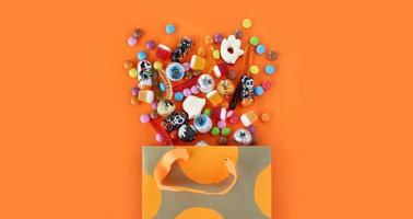 Shopping paper orange polka dot gift bag full of spilled assorted traditional Halloween candies. Orange banner background with copy space. Happy Halloween holiday sale and trick or treat concept. photo