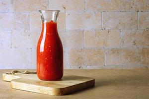 A glass jar bottle with homemade tomato sauce stands on a wooden cutting board photo