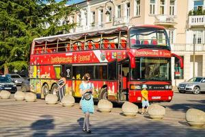 Batumi, Georgia, 2022 - female tourist walk us phone in street pass red two floor double-decker classic sightseeing bus around city. Famous city attraction photo