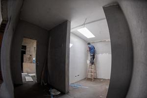 trabajador de la construcción usando una escalera mientras enyesaba paredes de yeso foto