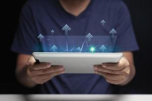 Tablet in hand of a man looking at a holographic digital business growth chart in his home. Small Business Ideas. selective focus on tablet. photo