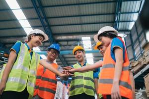 Group of industrial warehouse asian worker in safety suite hand stack celebrate successful or deal commitment. Logistics , supply chain and warehouse business.Teamwork unity under view concept. photo