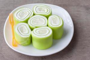 Young coconut pandan roll cake in white plate on vintage wooden table background. photo