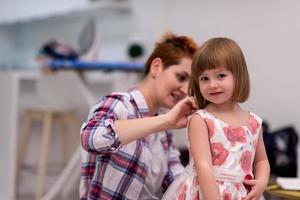 mother helping daughter while putting on a dress photo