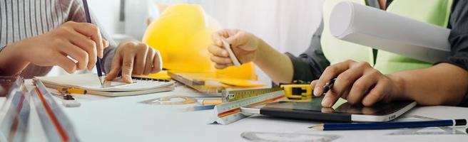 Two colleagues discussing data working and tablet, laptop with on on architectural project at construction site at desk in office photo