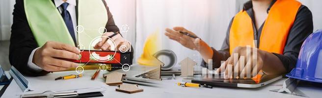 Two colleagues discussing data working and tablet, laptop with on on architectural project at construction site at desk in office photo