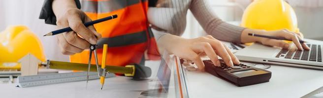Two colleagues discussing data working and tablet, laptop with on on architectural project at construction site at desk in office photo