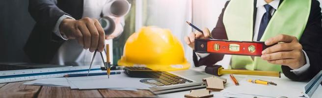 Two colleagues discussing data working and tablet, laptop with on on architectural project at construction site at desk in office photo