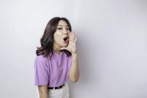 joven mujer hermosa con una camiseta morada lila gritando y gritando fuerte con una mano en la boca. concepto de comunicación foto