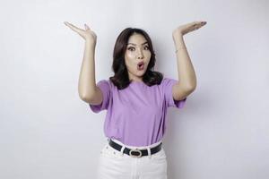 mujer asiática conmocionada con una camiseta morada lila que señala el espacio de la copia al revés, aislada de fondo blanco foto