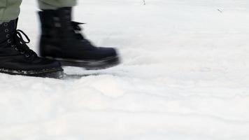 en kvinna promenader i de snö i en vinter- skog, stövlar lämna fotspår i de färsk snö. ben av en kvinna i svart stövlar, mystiskt och mystiskt gående i de snö i vinter. låg vinkel. video