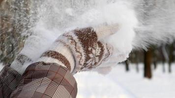 una hermosa joven irreconocible sopla nieve de sus palmas. la niña se encuentra entre el bosque de invierno y juega con la nieve en un día soleado. manos de mujer en mitones. camara lenta. video