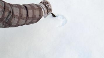 Female hands draw a romantic heart shape on light snow on a cold beautiful winter day. 4k. A young girl in mittens draws a heart with a stick on the snow outdoors, close-up. video