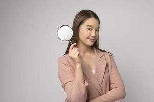 mujer asiática joven que sostiene la lupa sobre el concepto blanco del fondo, del análisis y de las finanzas. foto