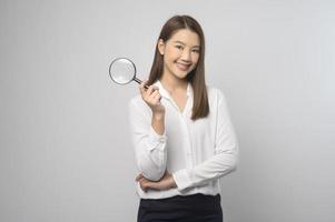 Young asian woman holding magnifying glass over white background, analysis and finance concept. photo